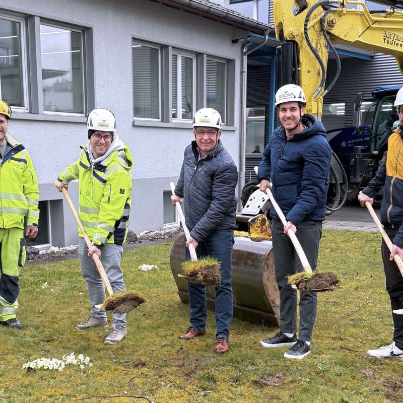 Die Mitglieder der GL halten je eine Schaufel mit Erde. Im Hintergrund steht ein Bagger.